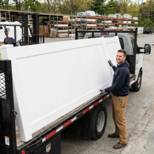 A smiling contractor loads high-quality factory-direct white vinyl fence panels onto a flatbed truck in a supply yard.